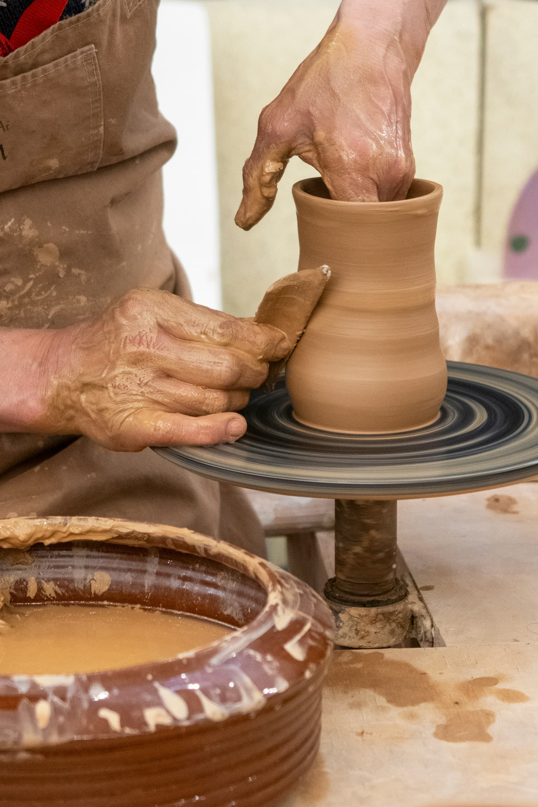 Hands shaping a clay pot on a potter's wheel
